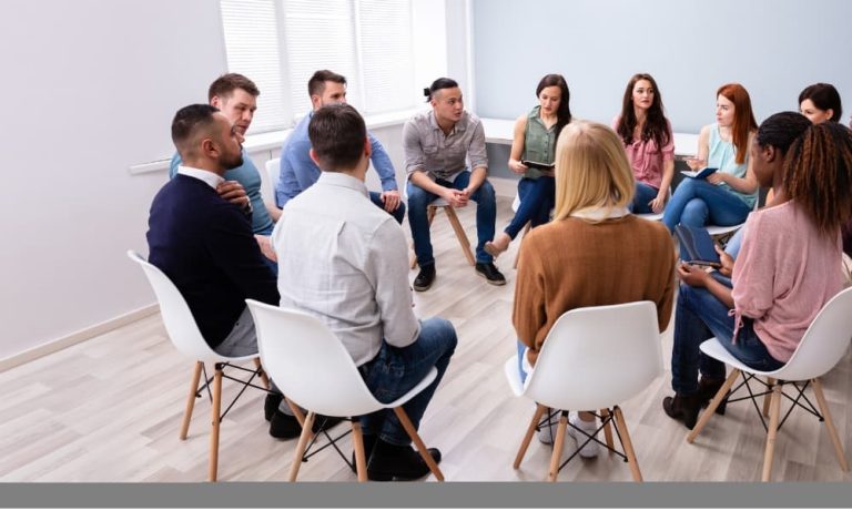 A group of people sitting in a circle on folding chairs having a group therapy session using CBT, DBT, and EMDR.