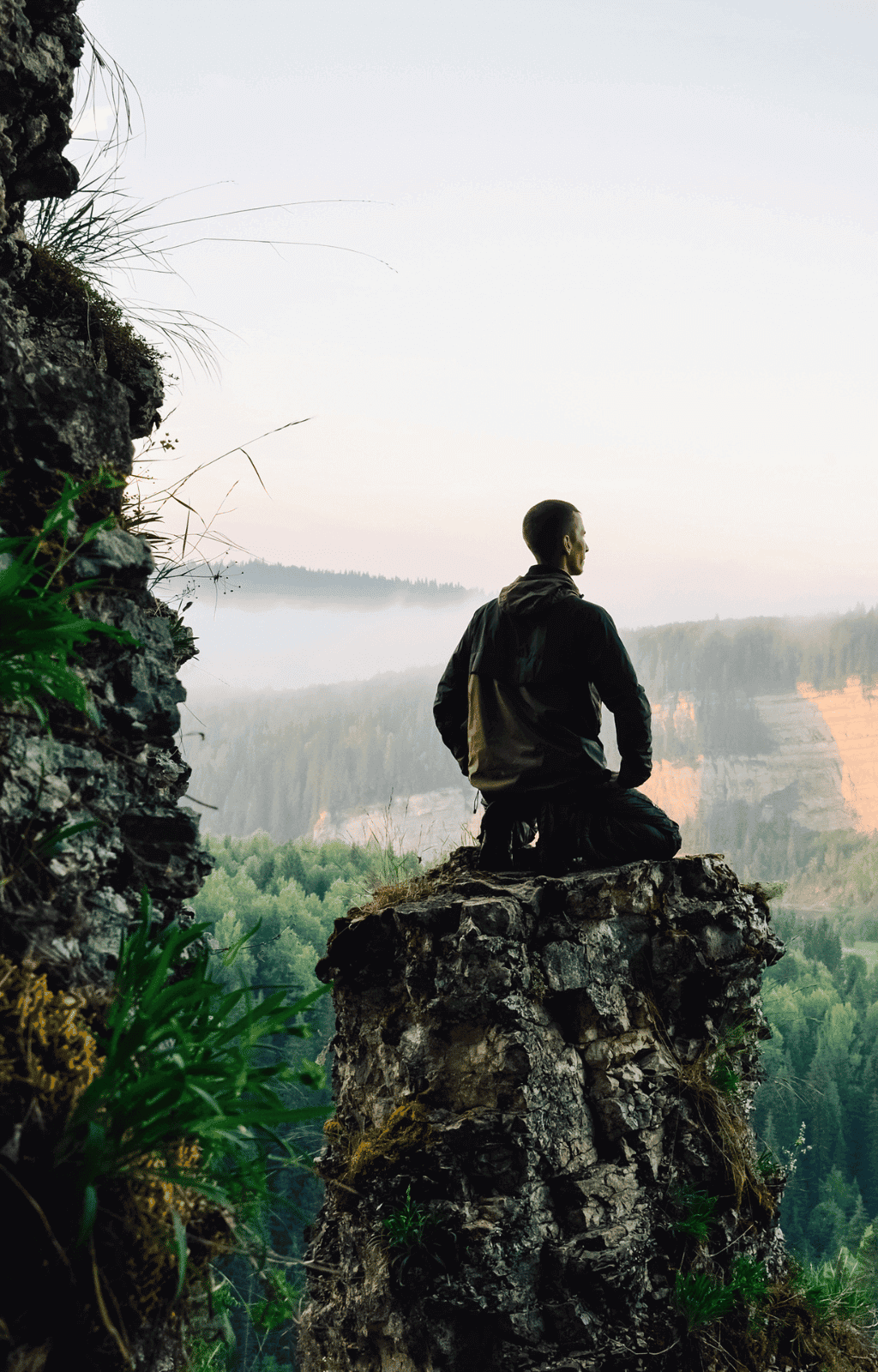 Person sitting on a cliff overlooking a forest